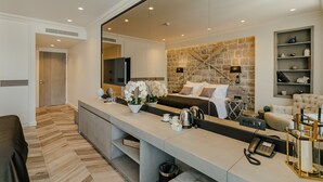 Une chambre d’hôtel moderne dotée d’un grand miroir, d’un mur décoratif en pierre, d’un canapé-lit, d’un bureau avec un téléphone et d’une petite plante.