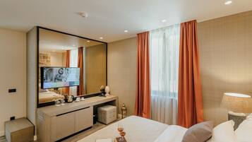 Una habitación de hotel moderna con una cama grande, una mesita de noche con una lámpara, un televisor, un escritorio con una computadora y un espejo amplio.