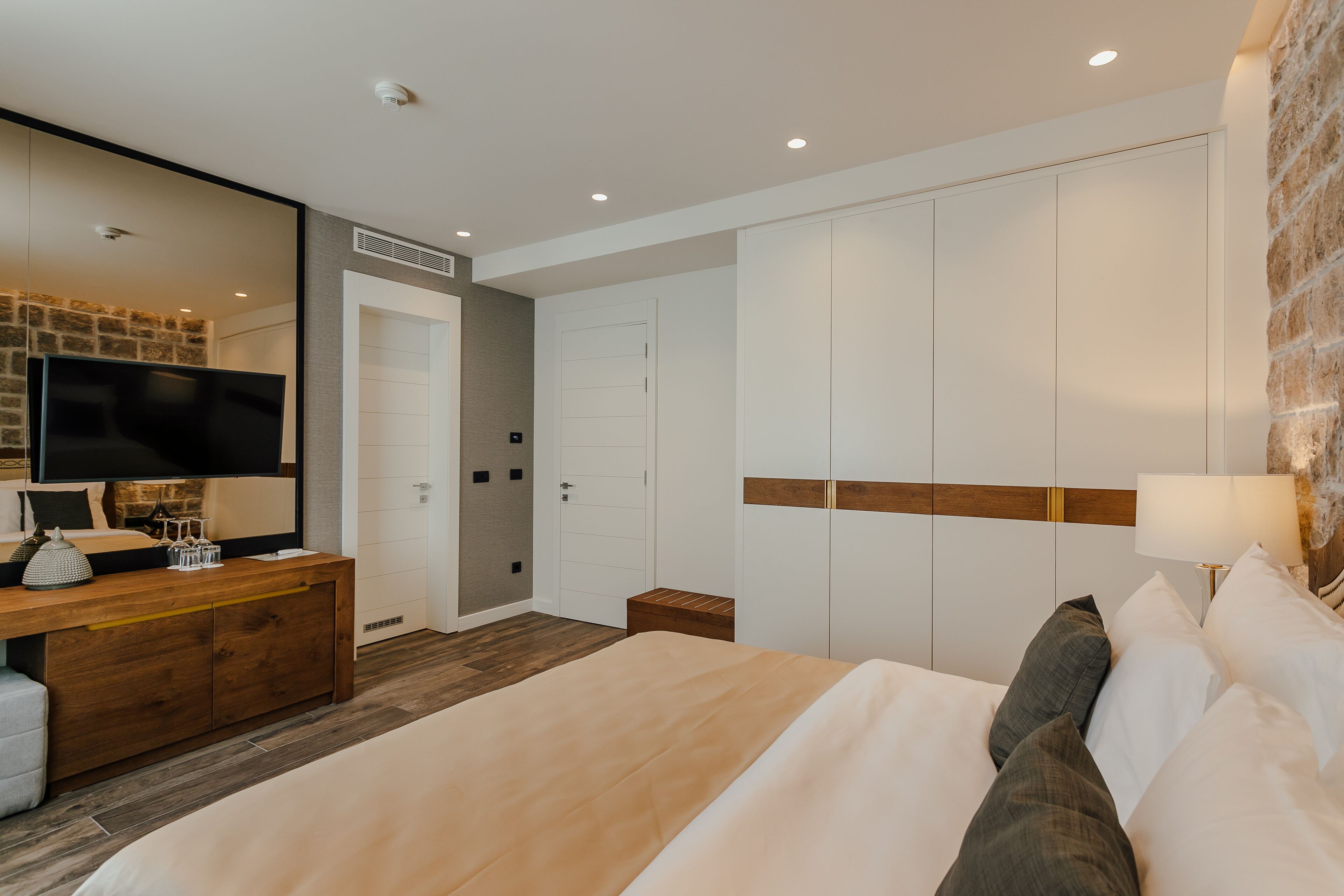 Een moderne hotelkamer met een groot bed, een houten dressoir, een flatscreen televisie en een accentmuur van steen.