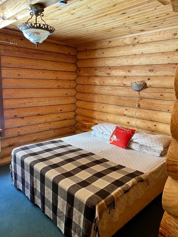 Un dormitorio de cabaña de madera acogedor, con cama, manta a cuadros y almohada roja.