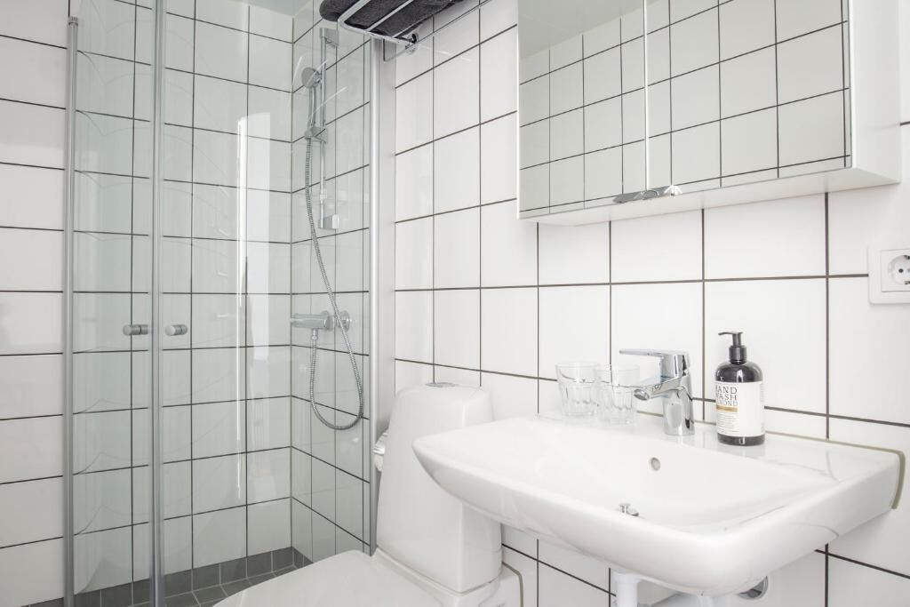 Un bagno moderno con cabina doccia in vetro, un lavandino bianco e uno specchio sopra il lavandino.