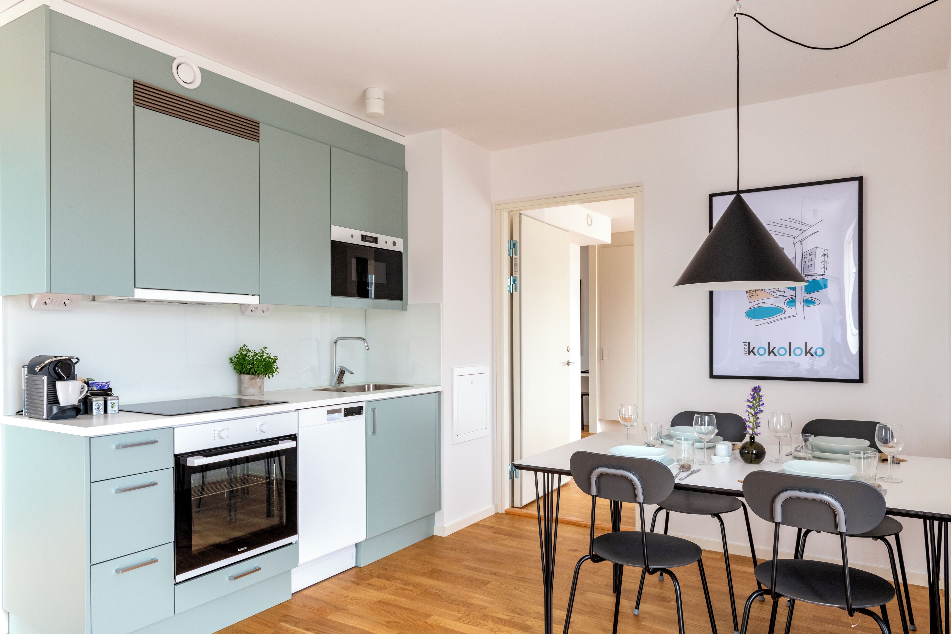 A modern kitchen with light blue cabinets, a built-in oven, and a dining area with a table set for four.