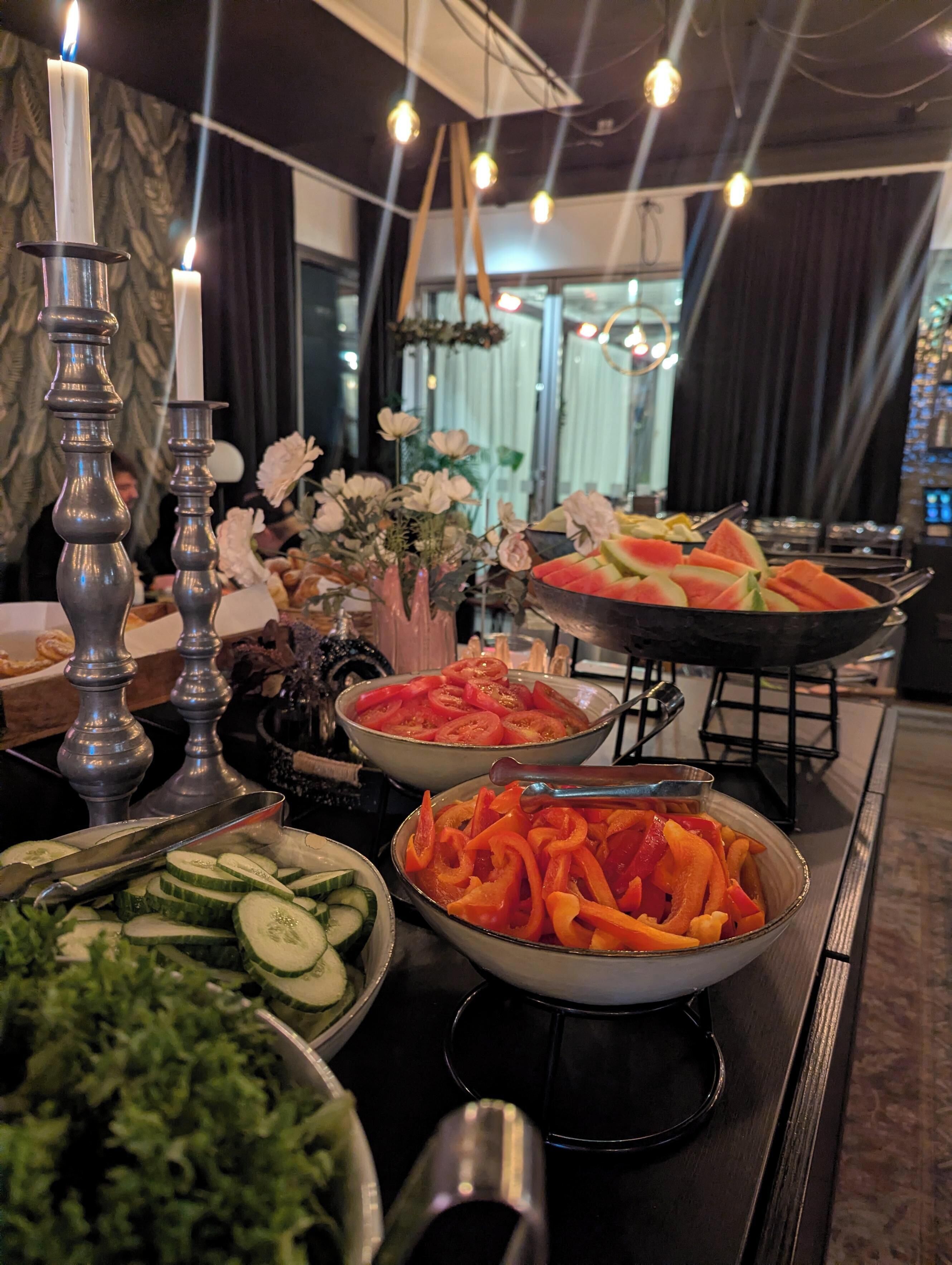 A buffet table with various food items, including sliced cucumbers, bell peppers, and watermelon.