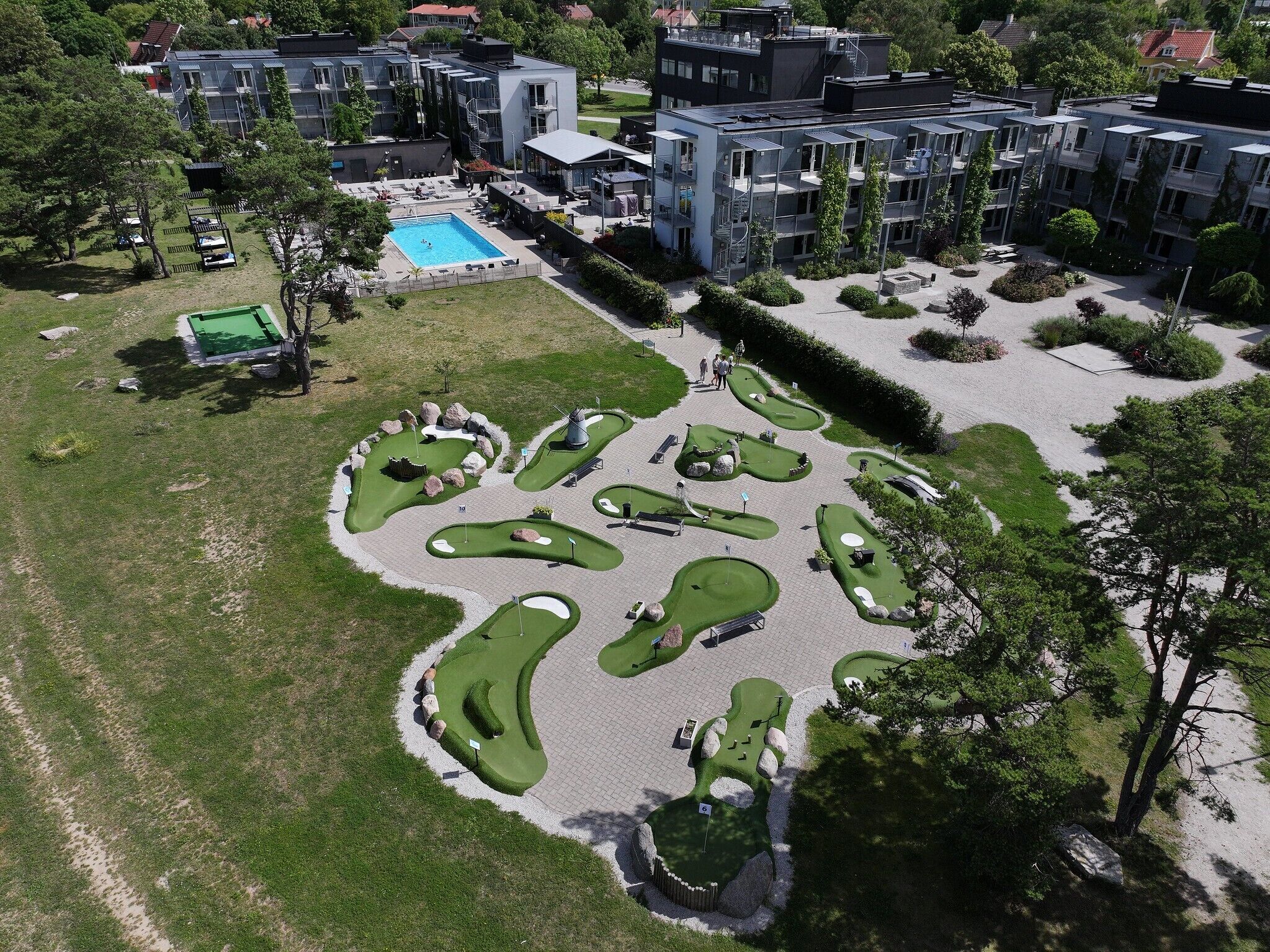 An aerial view of a residential area with modern apartment buildings, a swimming pool, and a golf course.
