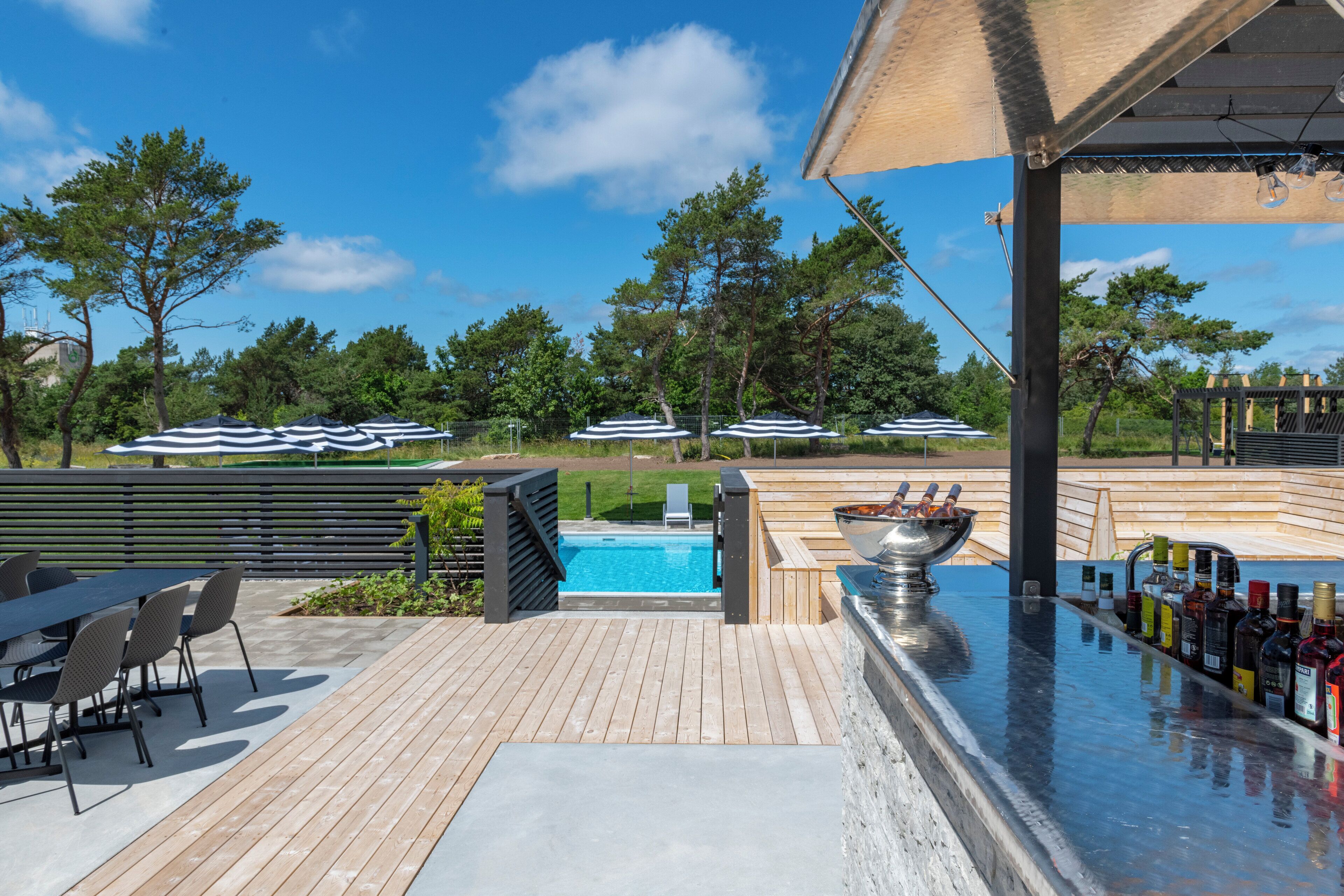 Una terraza de madera con piscina, mobiliario exterior y sombrillas.