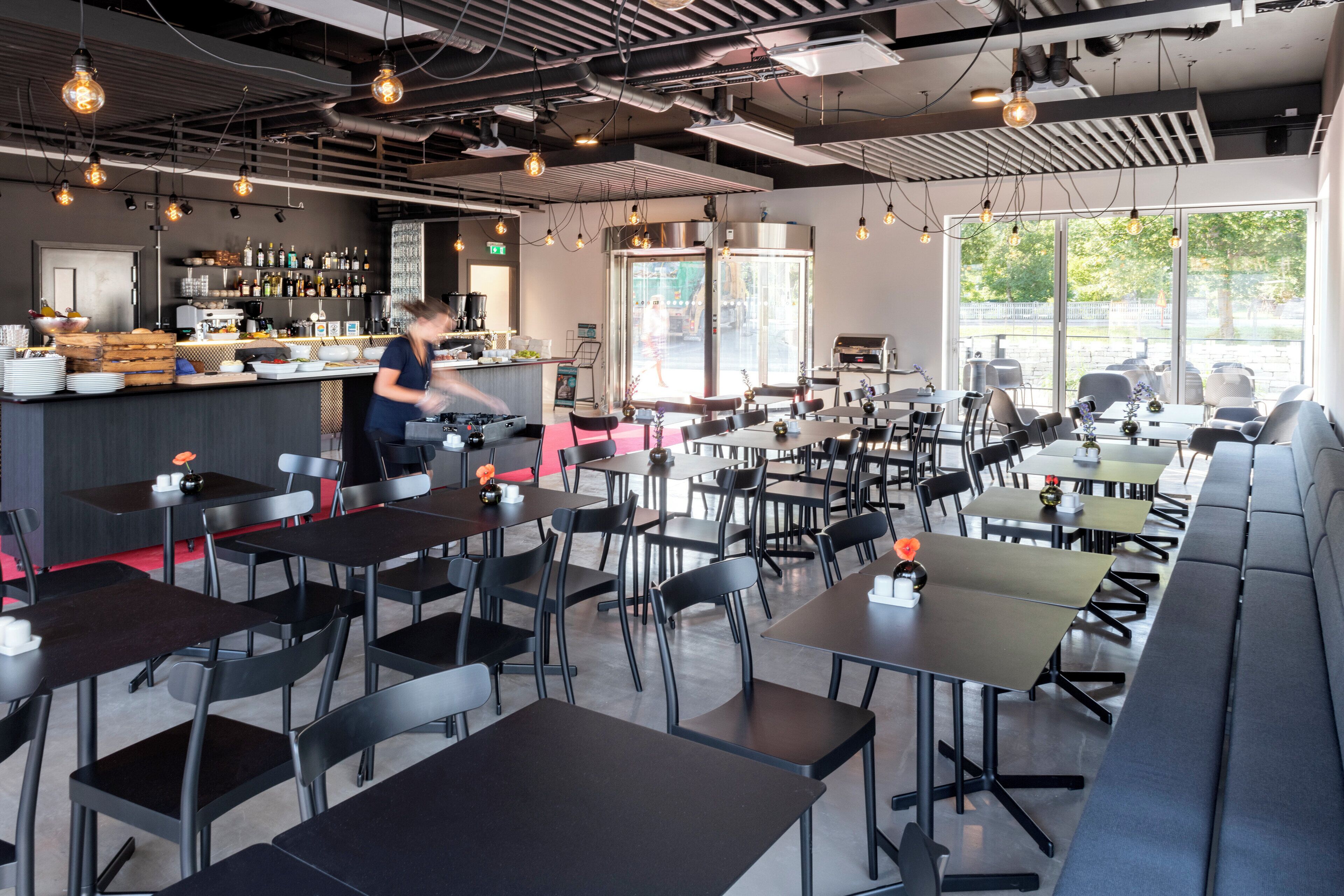 Un restaurant moderne doté d’un bar, de plusieurs types de sièges, notamment des tables et des banquettes, et offrant une vue sur l’extérieur grâce à de grandes fenêtres.