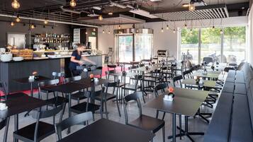 Un restaurante moderno con área de bar, diversas opciones de asientos, incluyendo mesas y cabinas, y vistas al exterior a través de amplios ventanales.