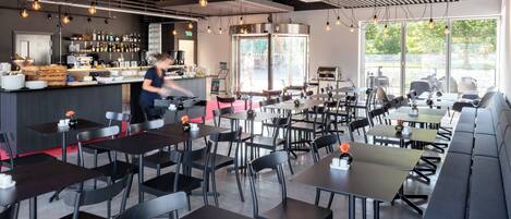 Un restaurant moderne doté d’un bar, de plusieurs types de sièges, notamment des tables et des banquettes, et offrant une vue sur l’extérieur grâce à de grandes fenêtres.