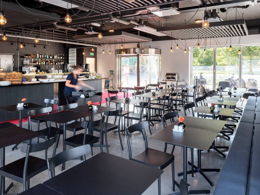 Un restaurante moderno con área de bar, diversas opciones de asientos, incluyendo mesas y cabinas, y vistas al exterior a través de amplios ventanales.