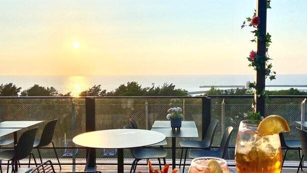 Une table dressée avec une salade, un bol de cocktail de crevettes et un cocktail décoré d’une tranche de citron, donnant sur une étendue d’eau au coucher du soleil.