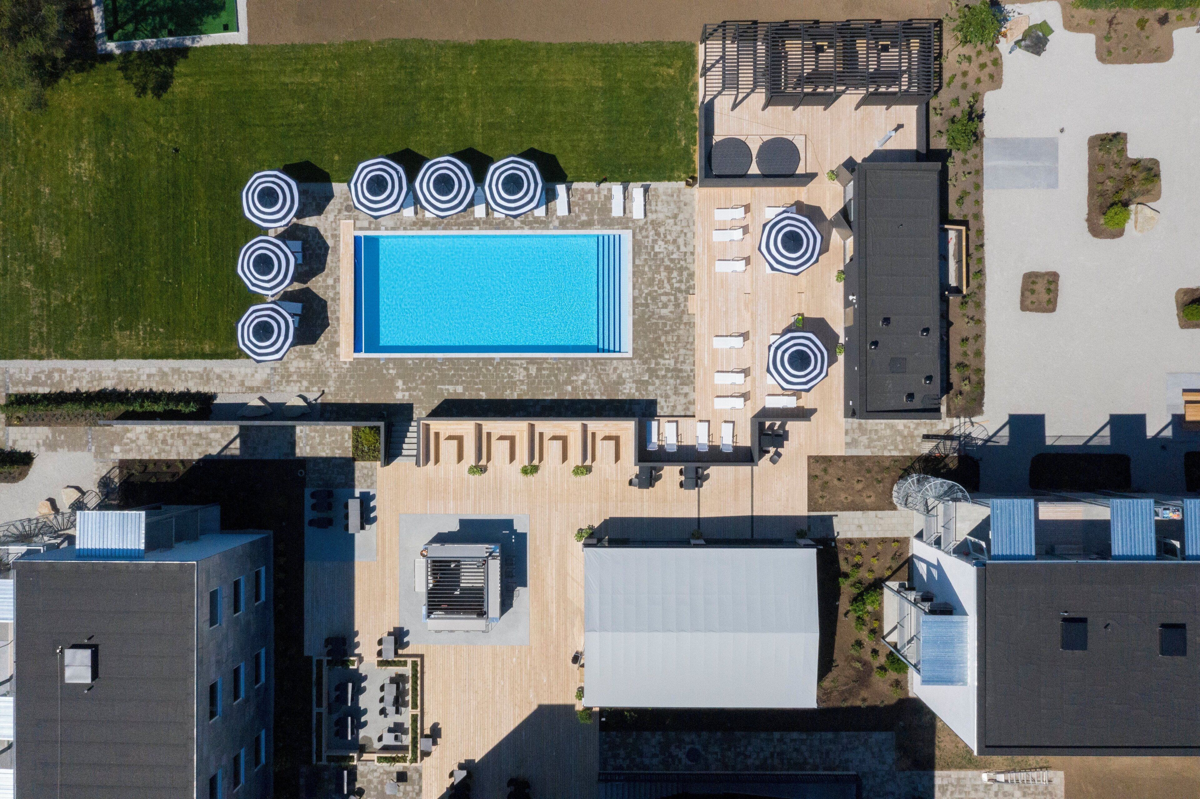 Vista aérea de un hotel con piscina central, zona de estar al aire libre con sombrillas y varias construcciones.