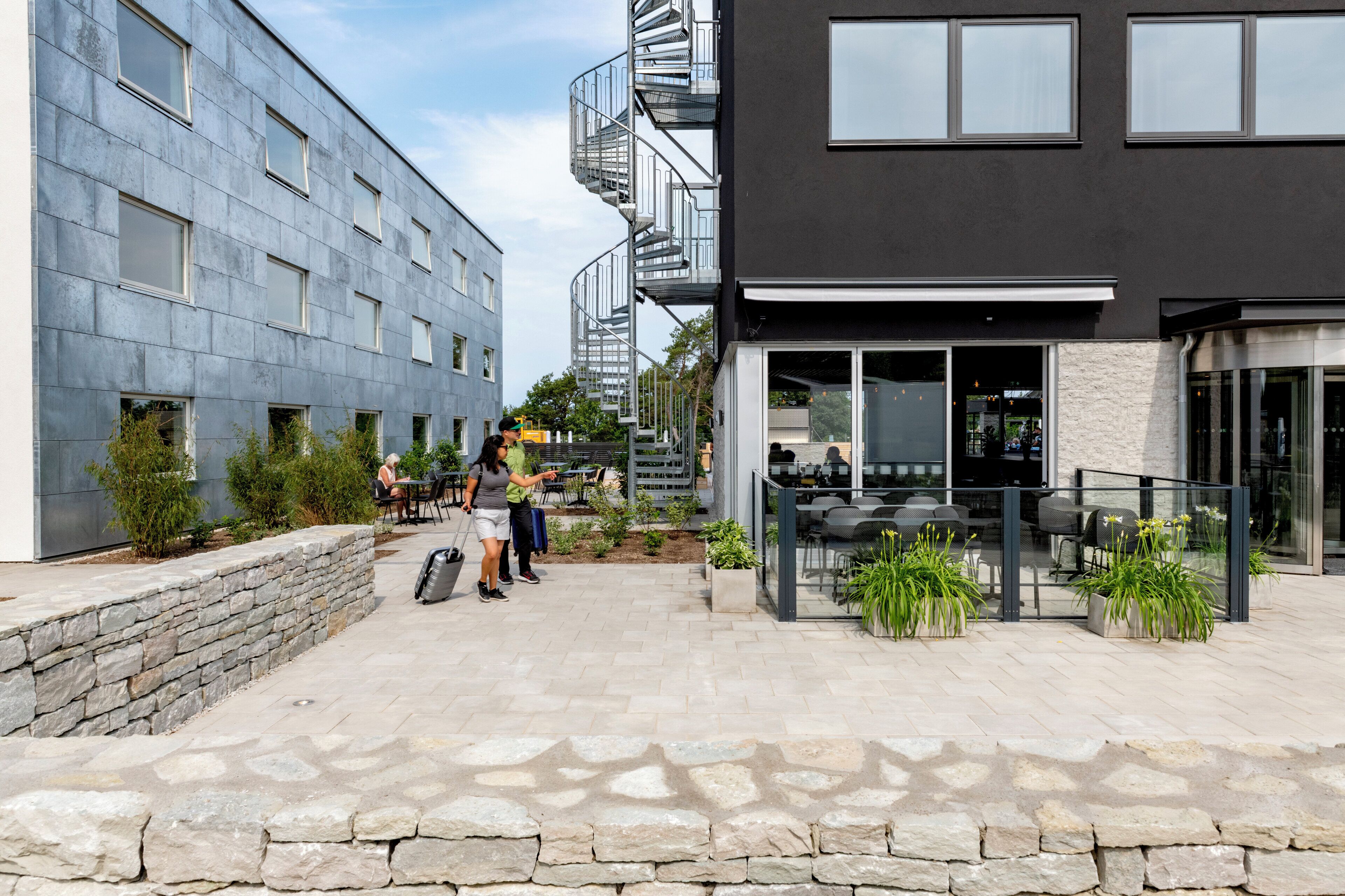 A modern building with a stone facade, outdoor seating area, and a spiral staircase.