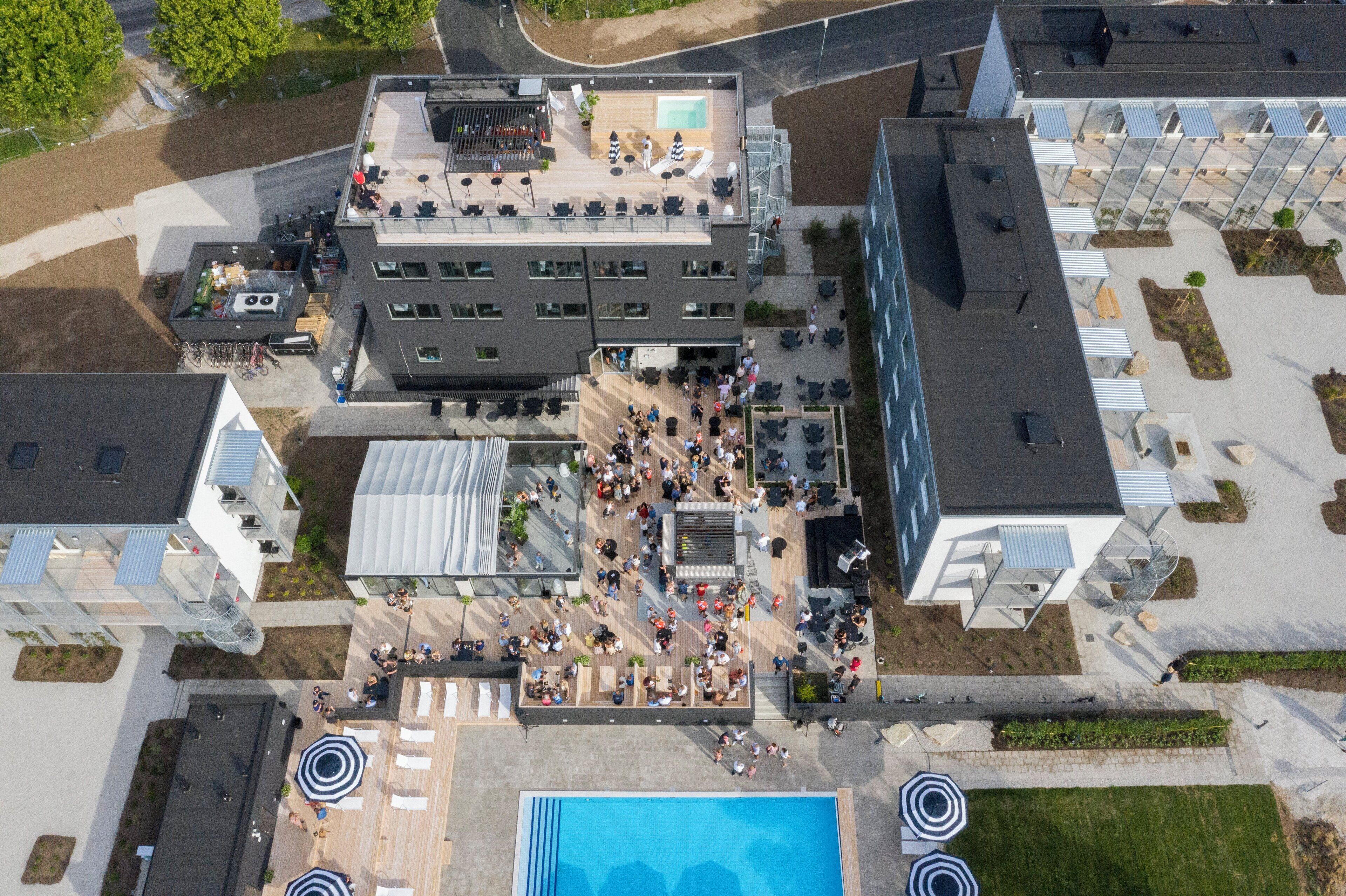 An aerial view of a modern building with a rooftop terrace, outdoor seating area, and a swimming pool.