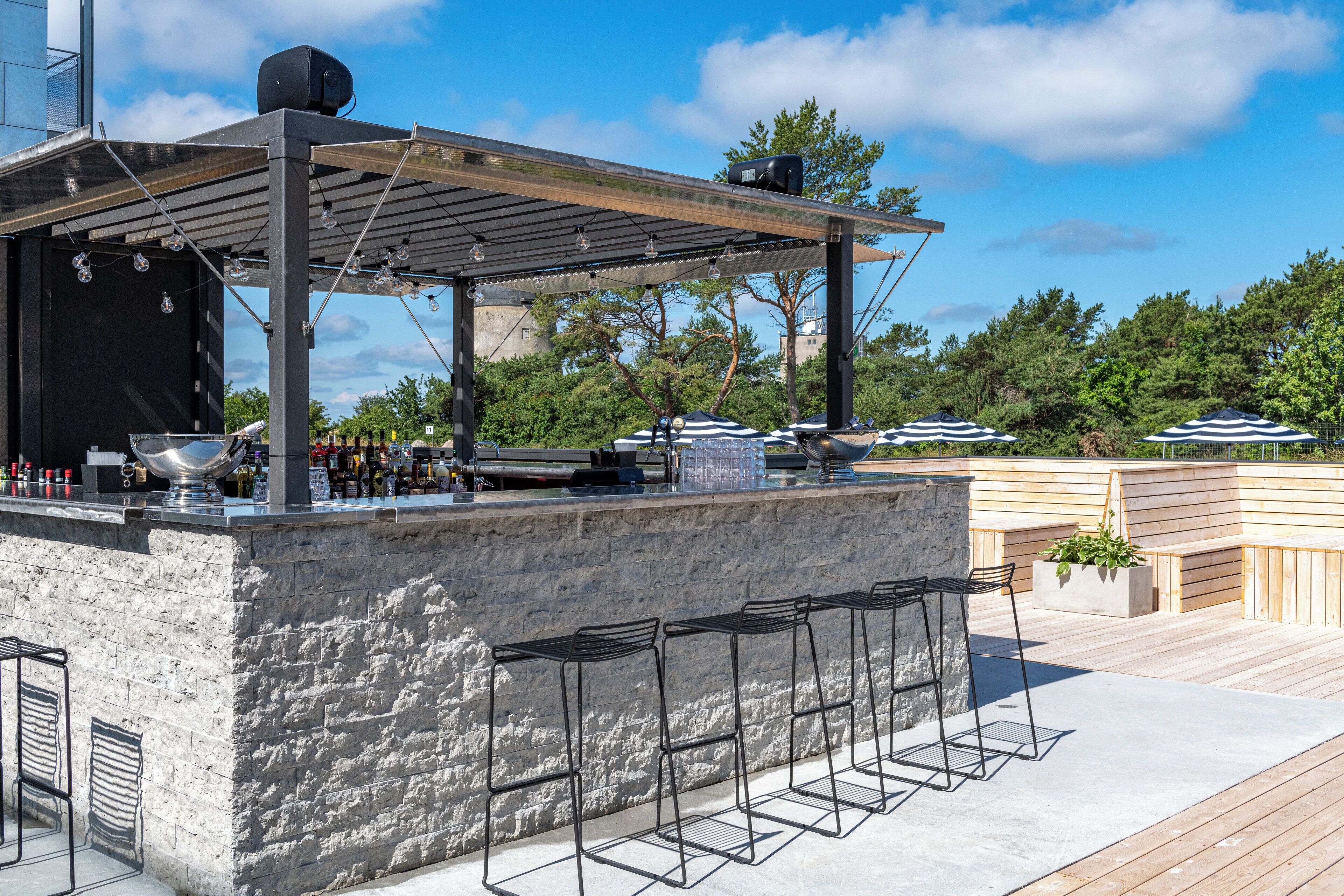 An outdoor bar area with a stone counter, metal bar stools, and a wooden deck.