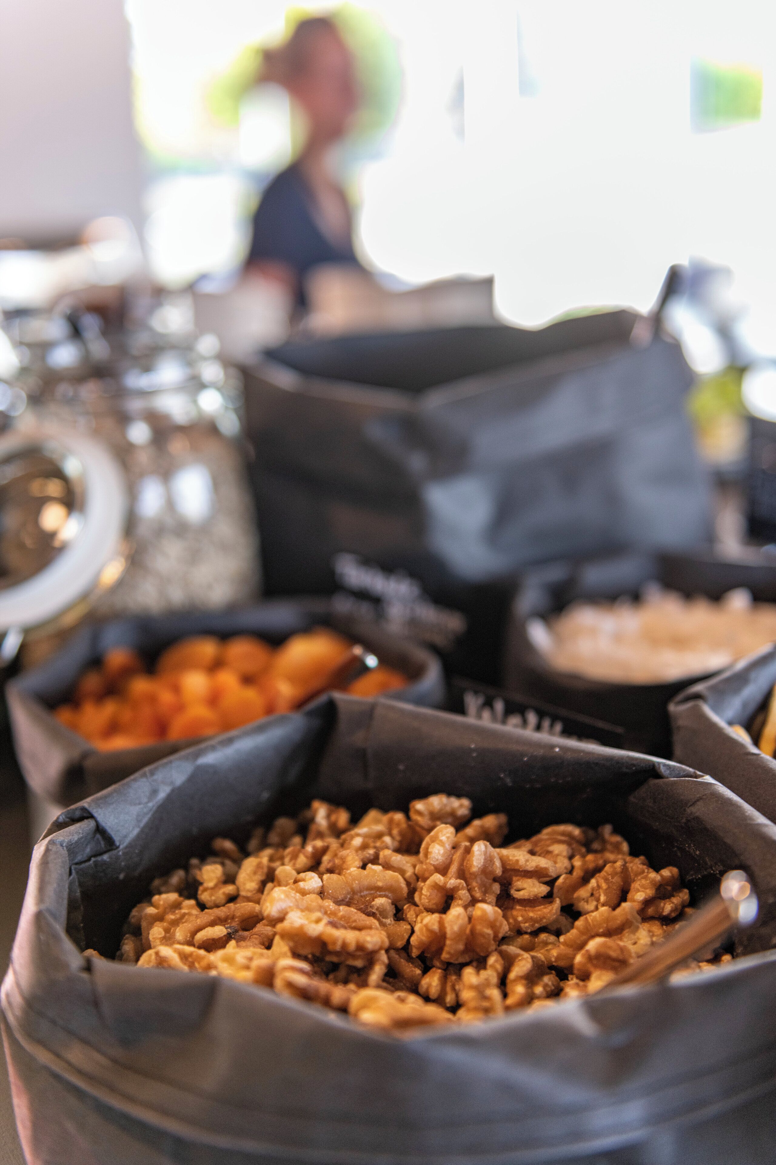 A close-up of bags filled with nuts, with a blurred background of a person and a coffee machine.