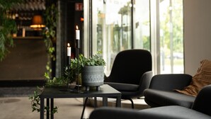 Un intérieur moderne avec un canapé noir, une petite table ornée de bougies et d’une plante en pot, et une grande fenêtre donnant sur l’extérieur.