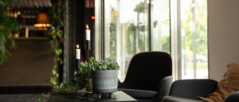 Un interior moderno con un sofá negro, una mesita con velas y una planta en maceta, y un amplio ventanal con vistas al exterior.