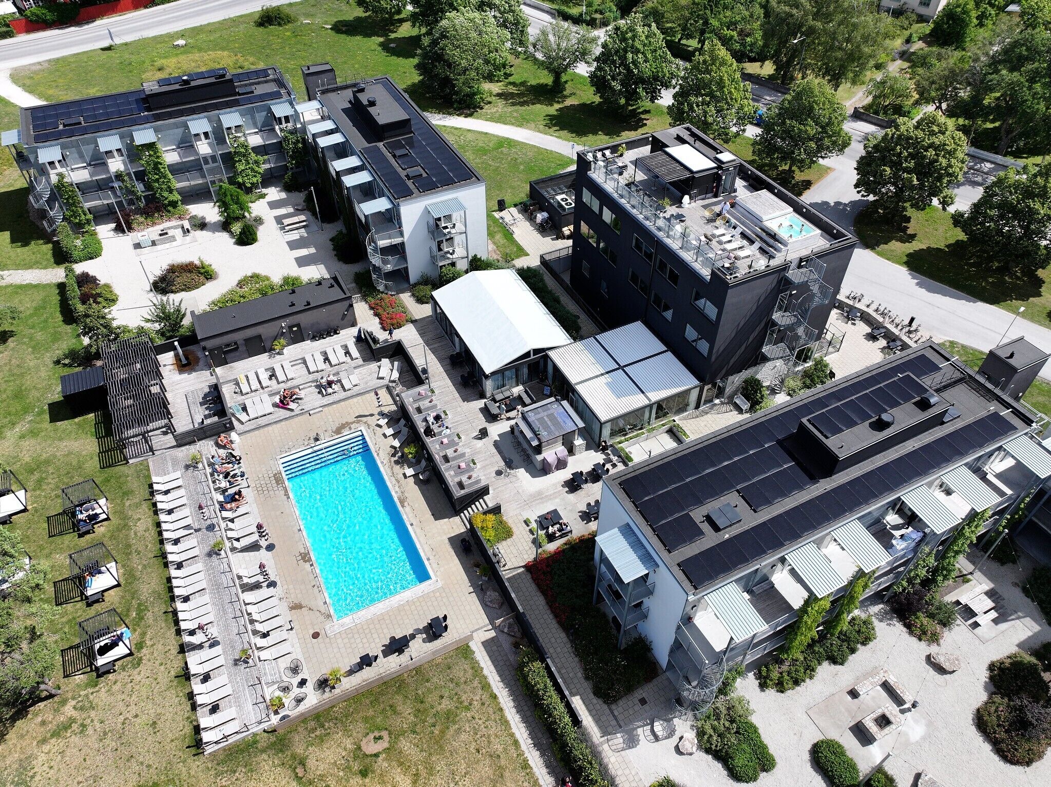 En vy från ovan av ett modernt byggnadskomplex med en swimmingpool, utomhusmöbler och solpaneler.