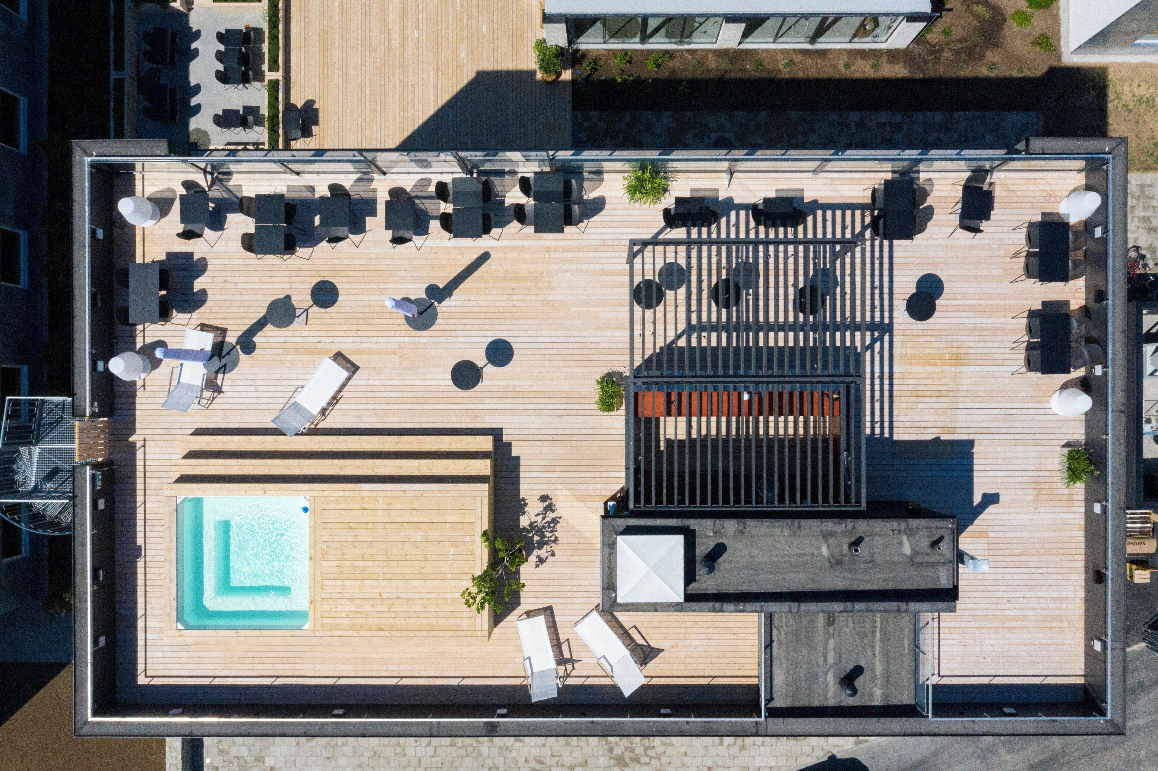 An aerial view of a rooftop terrace with a swimming pool, multiple seating areas, and a bar.