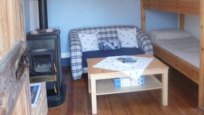 Una habitación de cabaña acogedora con interior de madera, un sofá, una cama nido y un estufa de leña.