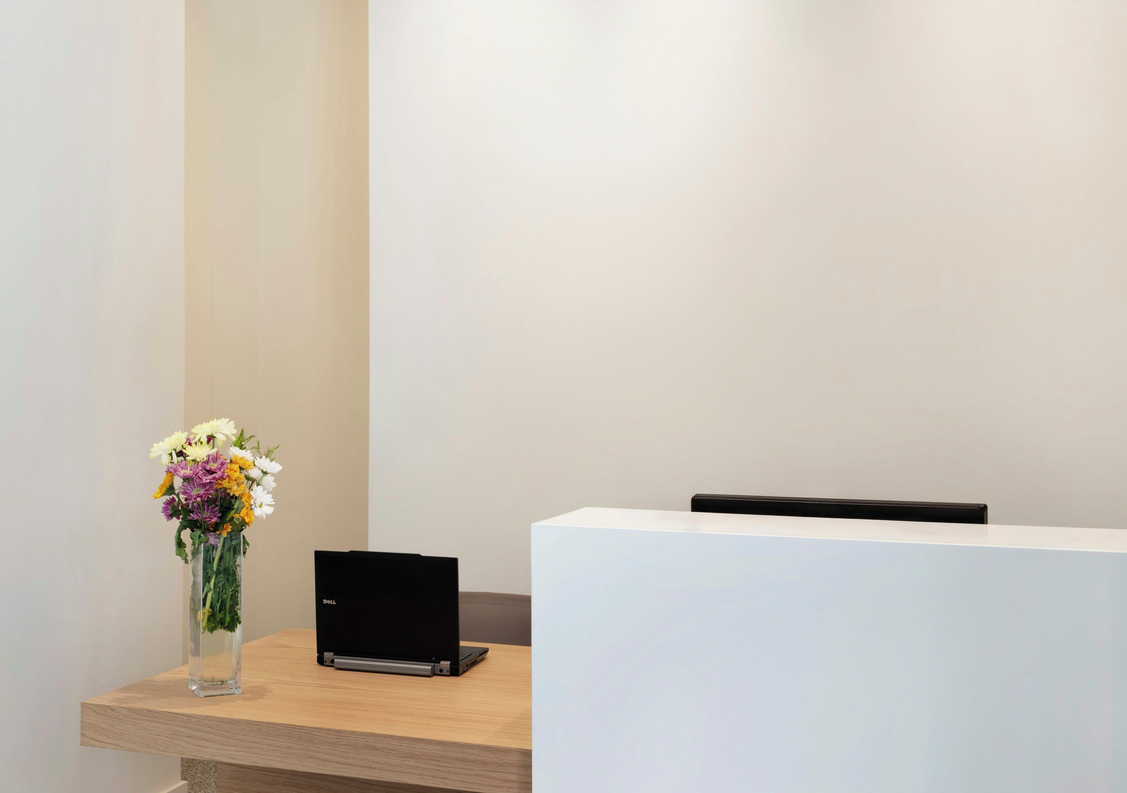 Un comptoir d’accueil avec un ordinateur portable et un vase de fleurs.