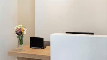 Un comptoir d’accueil avec un ordinateur portable et un vase de fleurs.
