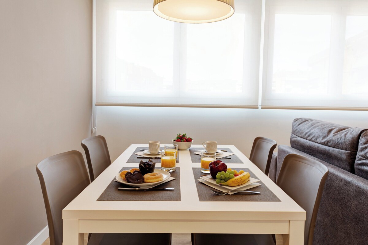 A dining table with breakfast items, a bowl of fruit, and a coffee cup.