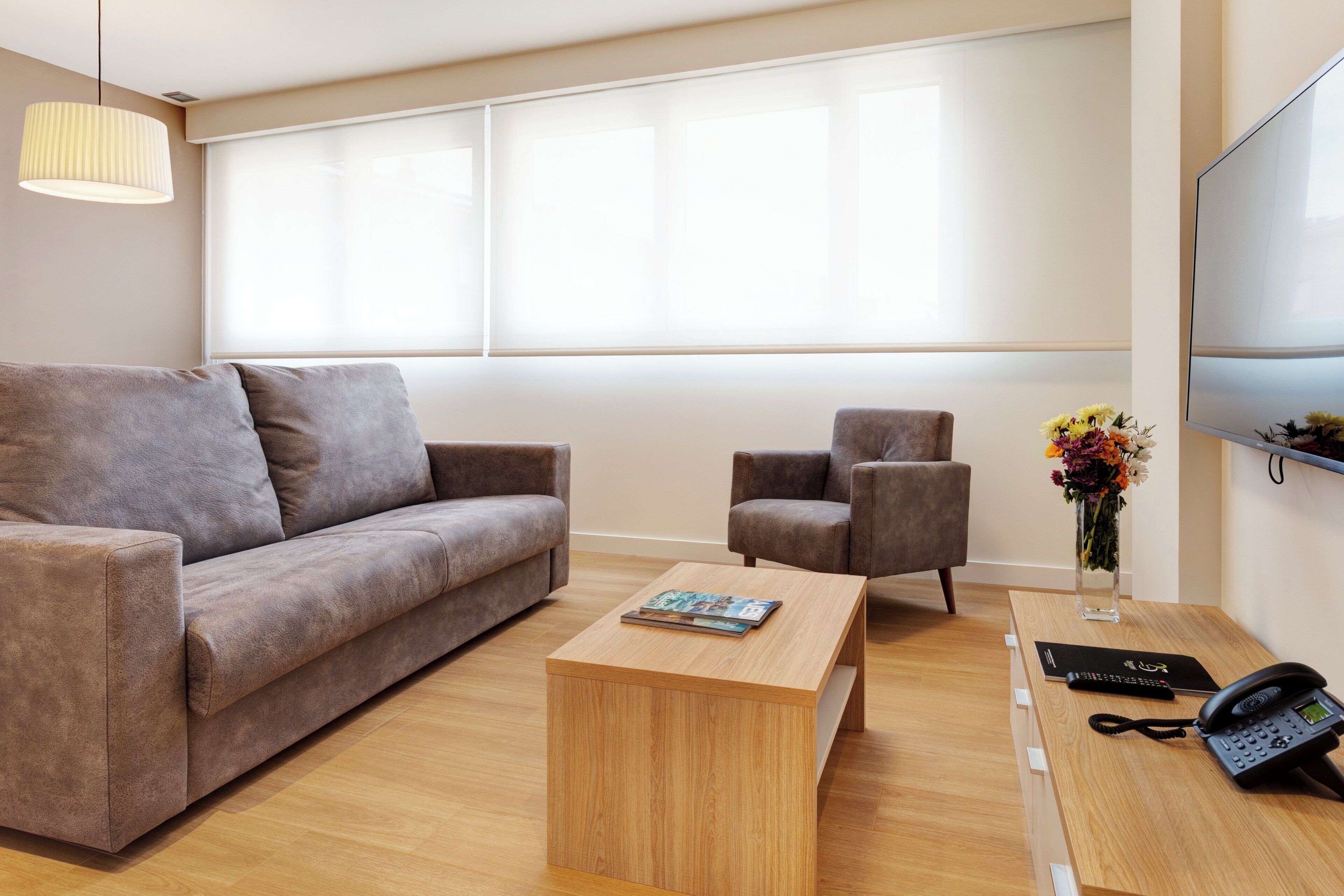 Una sala de estar moderna con un sofá, un sillón, una mesa de centro y un televisor de pantalla plana.