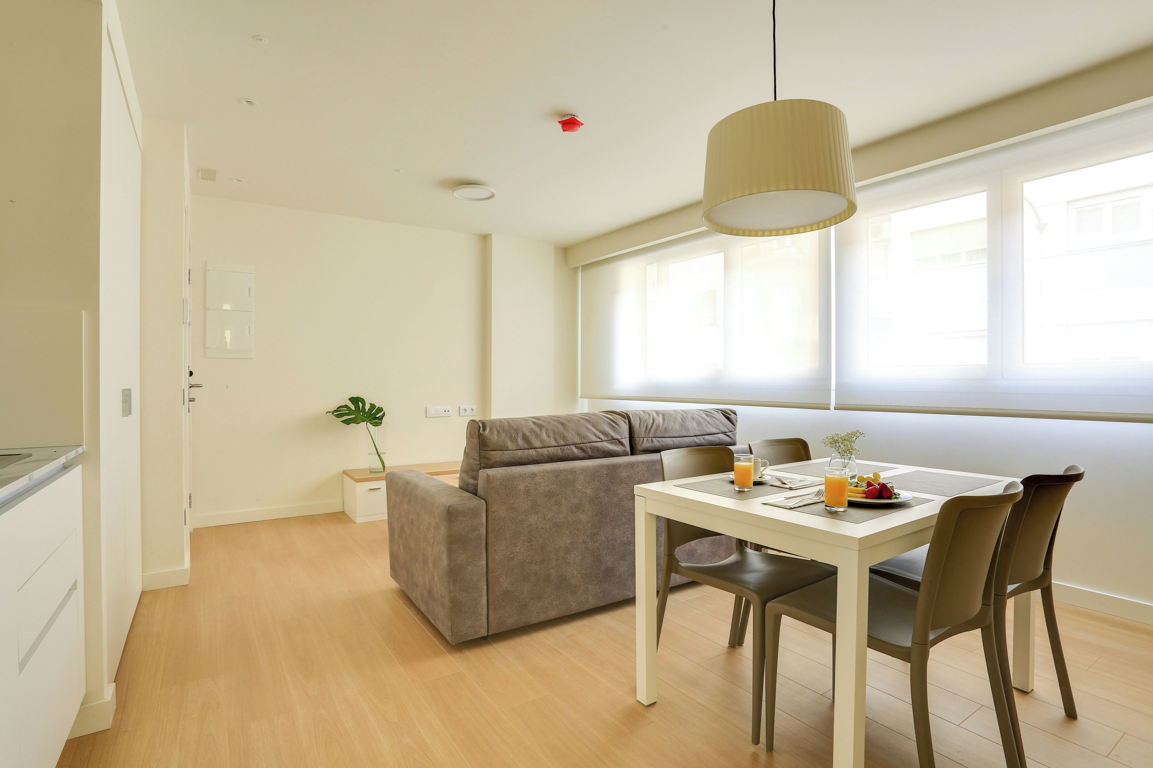 A modern, well-lit room with a dining table, chairs, a sofa, and a hanging light fixture.