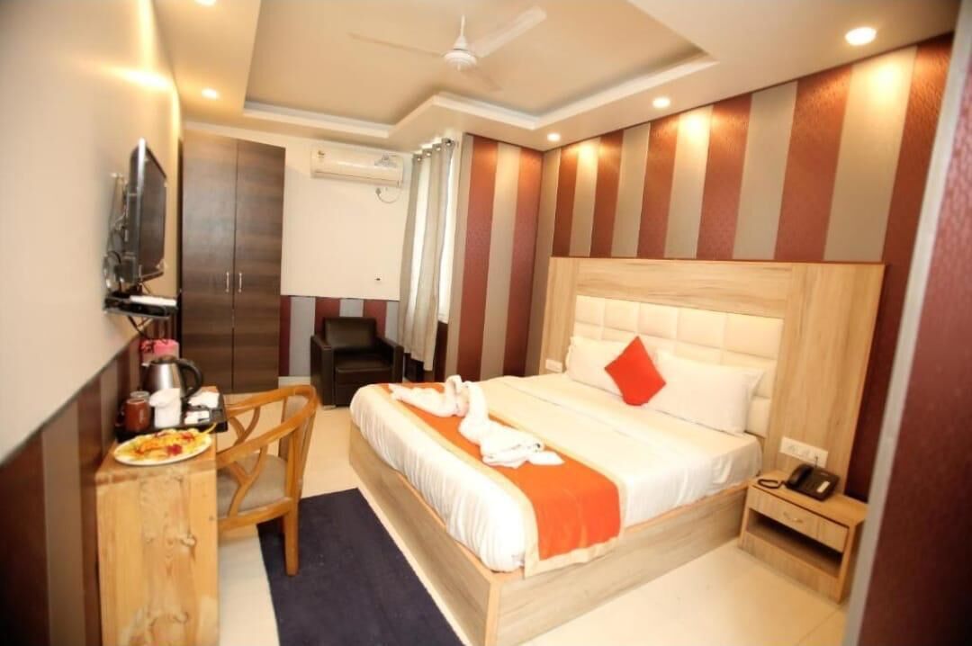 Habitación de hotel con una cama, un escritorio de madera, una silla, una mesita con un plato de comida, un teléfono y un ventilador de techo.