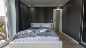 A modern bedroom with a large bed, a dark wall, and a sliding glass door leading to an outdoor area. - Apart Orkana 10 D Zakopane (Zakopane)