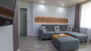 A modern living room with a grey sectional sofa, a wooden accent wall, and a flat-screen TV mounted on the wall. - Apart Orkana 10 D Zakopane (Zakopane)