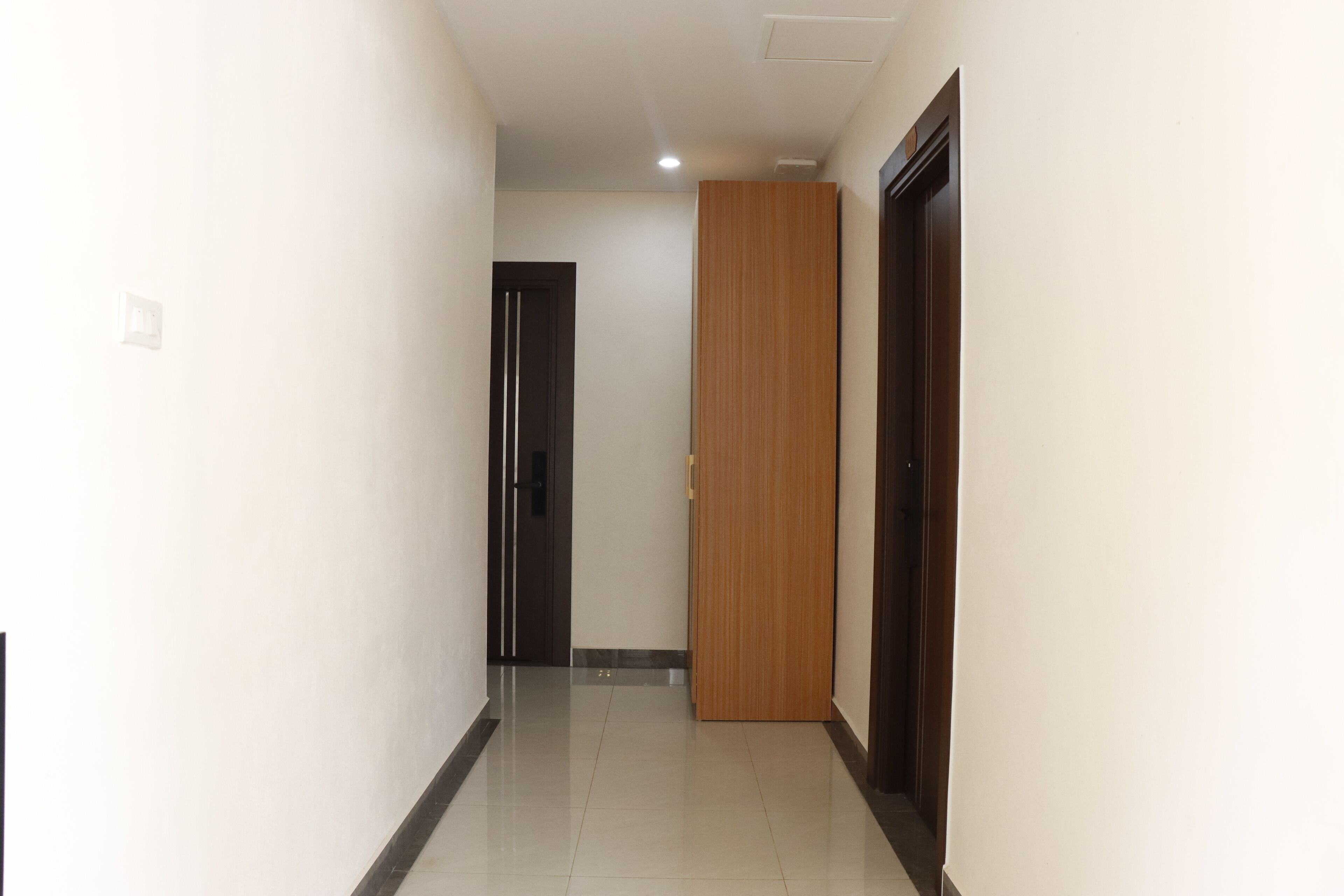 A hallway with a wooden door, a black door, and a light switch on the wall.