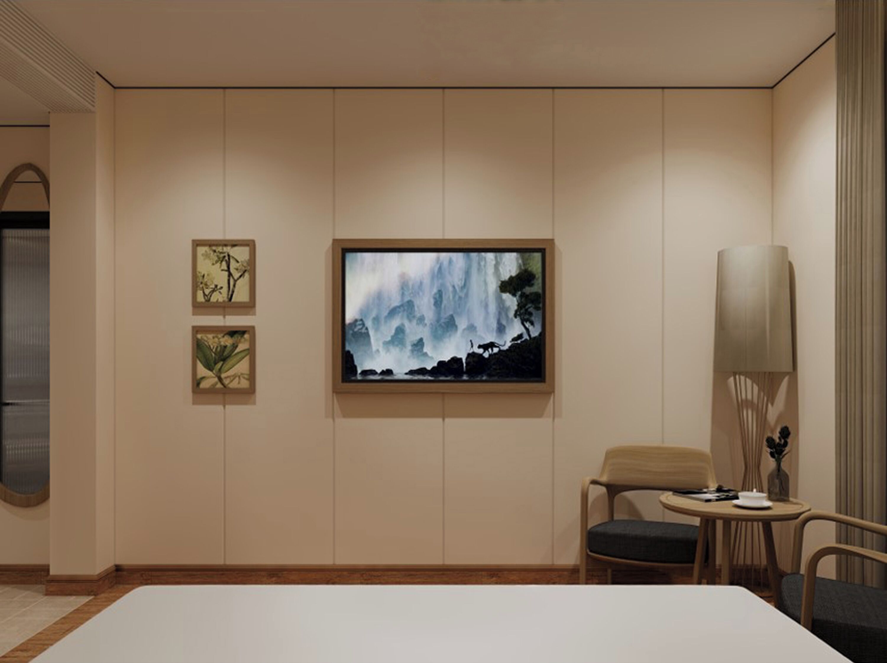 A modern hotel room with a large wall-mounted TV, two framed artworks, a round table with a chair, and a tall floor lamp.