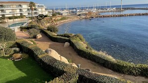 Une vue sur la côte, avec un port de plaisance, une piscine et un espace paysager agrémenté de rochers et d’arbustes.