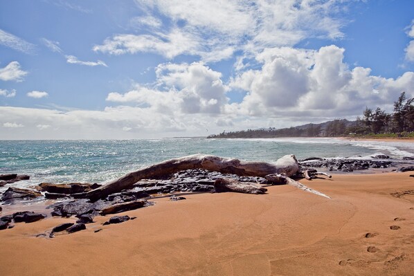A beach with a large rock formation in the foreground, a sandy shore, and the ocean in the background.