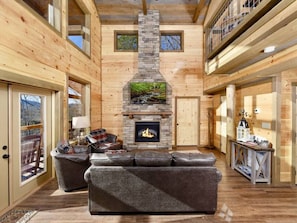 Cozy living room with a central fireplace, comfortable sofas, and a large window offering a view of the outdoors.