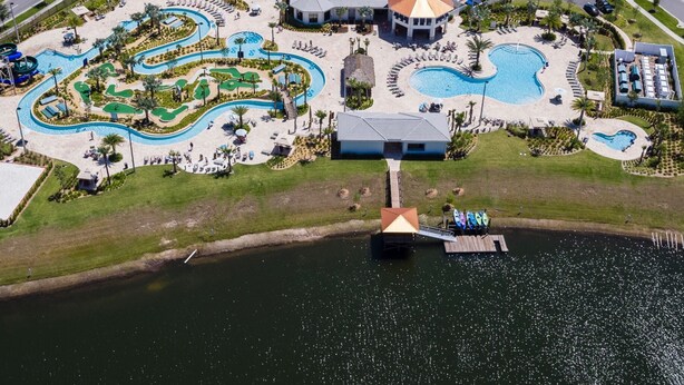 Ett flygbildsfoto av ett semesterområde med flera pooler, en vattenrutschkana och en brygga med båtar.