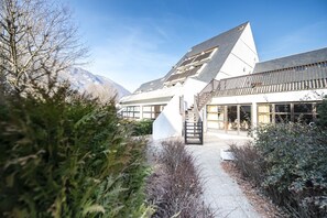 A modern building with a sloped roof, large windows, and a staircase leading to the entrance. - Les Ramondies - Vacances ULVF (Saint-Lary-Soulan)