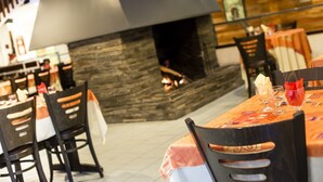 Ein Restaurant mit einem Kamin aus Stein, Holztischen und schwarzen Stühlen.