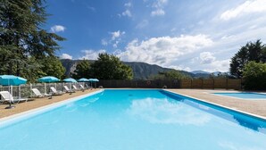 A swimming pool with lounge chairs and umbrellas, surrounded by trees and mountains in the background.