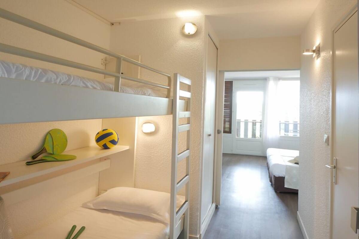 Un pasillo estrecho con literas a un lado y una puerta que da a otra habitación.