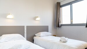 Une chambre d’hôtel avec deux lits, chacun doté de draps et d’oreillers blancs, d’une tête de lit et d’une fenêtre avec des rideaux.