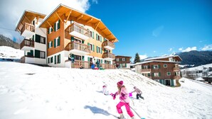 A multi-story wooden building with balconies, set against a snowy landscape with mountains in the background. - Les Essertets - Vacances ULVF (Praz-sur-Arly)