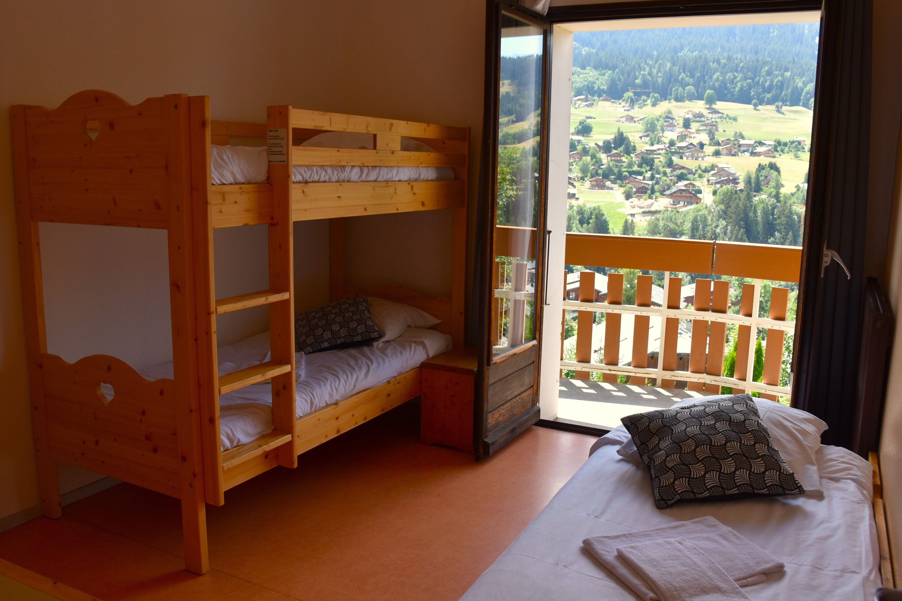 Una stanza con un letto a castello, un letto singolo e un balcone vista villaggio.