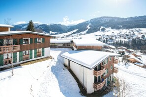 Vila coberta de neve com edifícios de madeira e montanhas ao fundo.