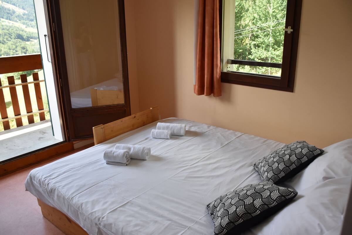 A bedroom with a wooden bed, white linens, two patterned pillows, and a window with curtains.