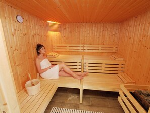 Uma sala de sauna com bancos de madeira, um relógio na parede e um balde.