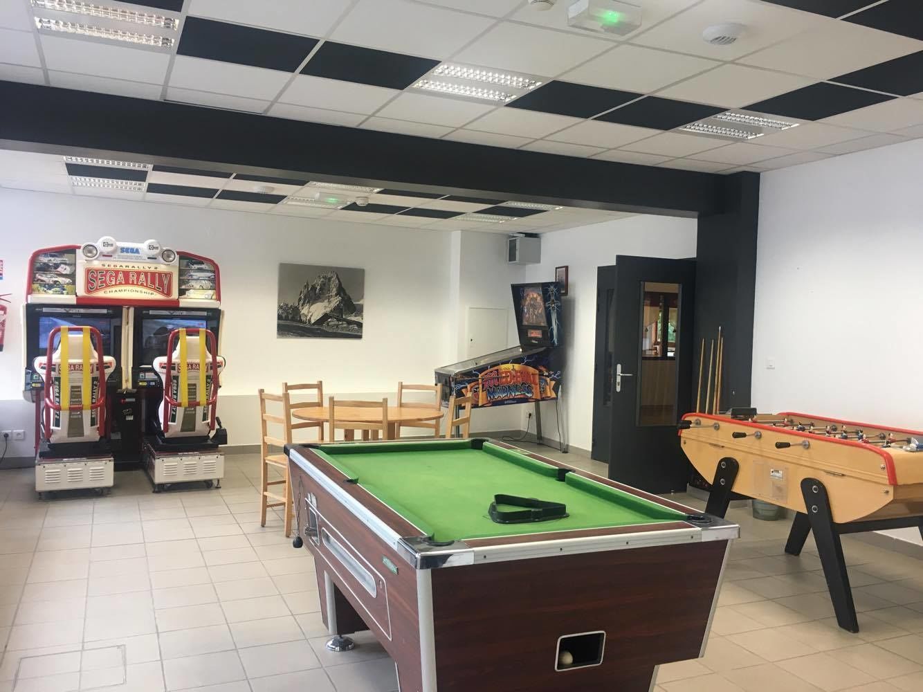 Una sala de billar con mesa de billar, dos mesas de fútbol de mesa y dos máquinas de arcade.