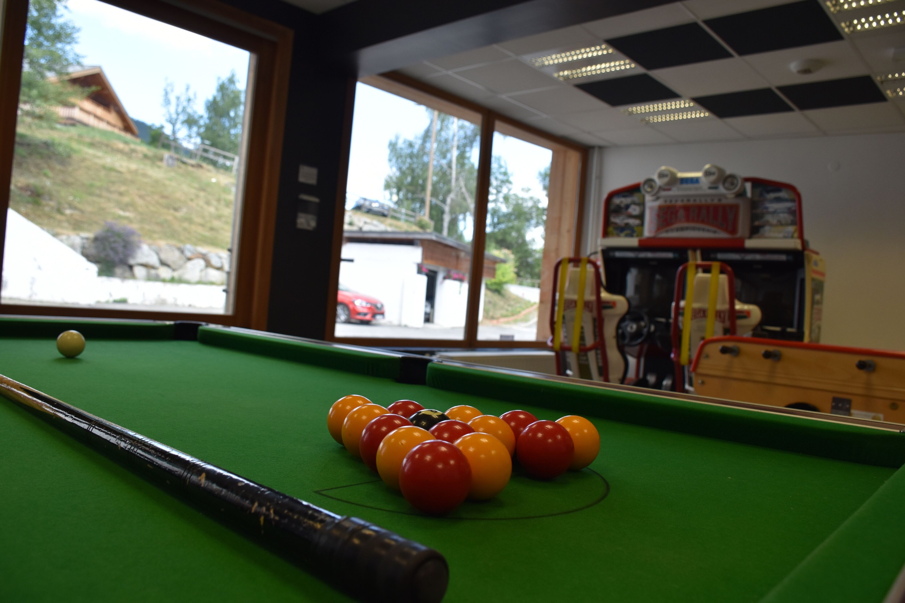 A pool table with balls, a pool cue, and a view of a building outside.